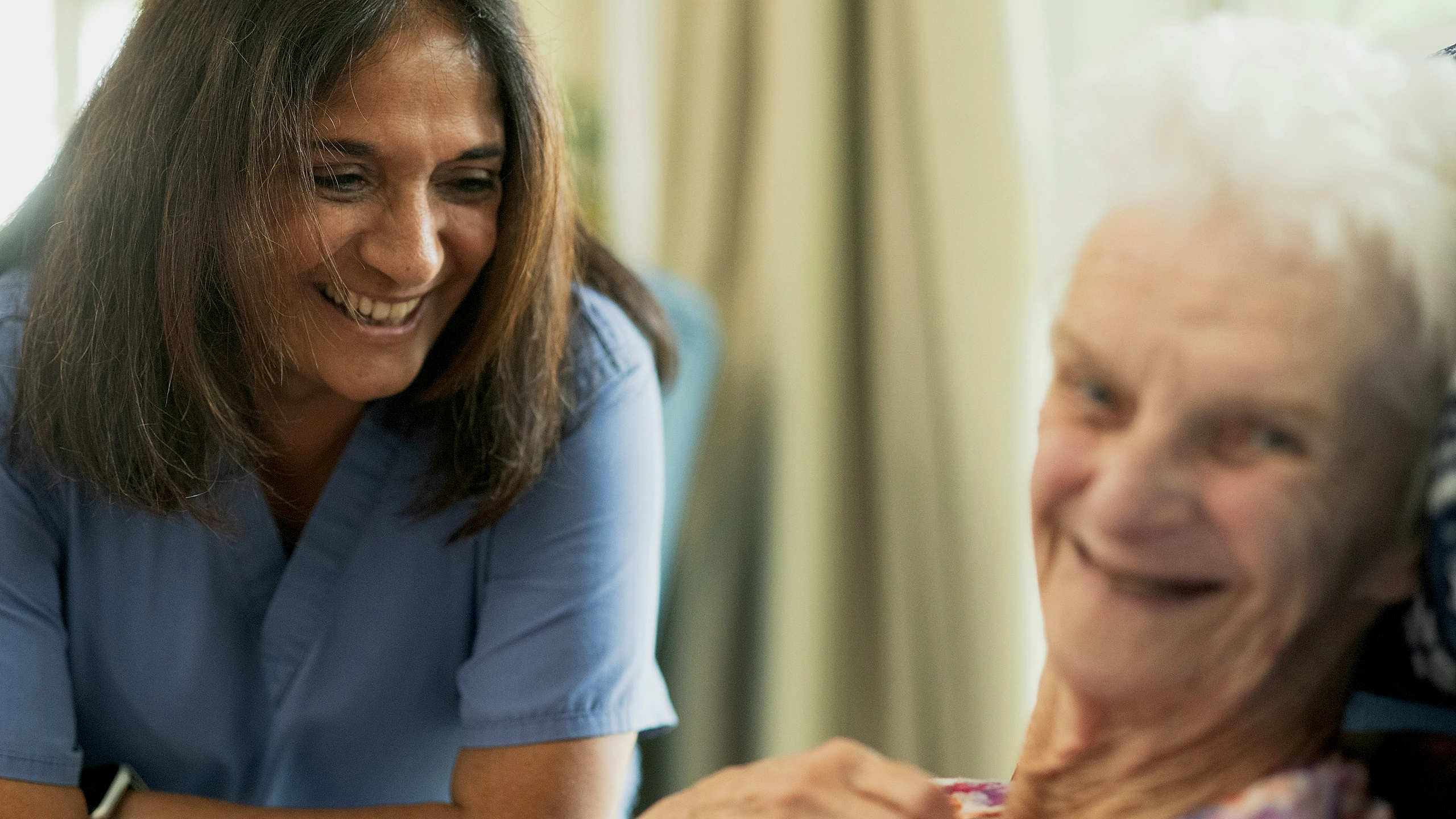 Care professional smiling with an older woman indoors